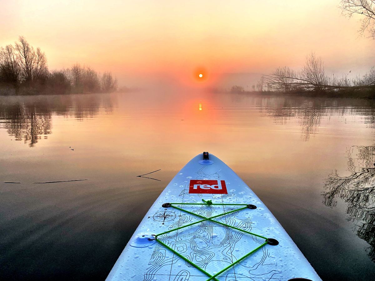 Het voorste deel van een SUP-board op de rivier met laaghangende mist en de zonsopkomst