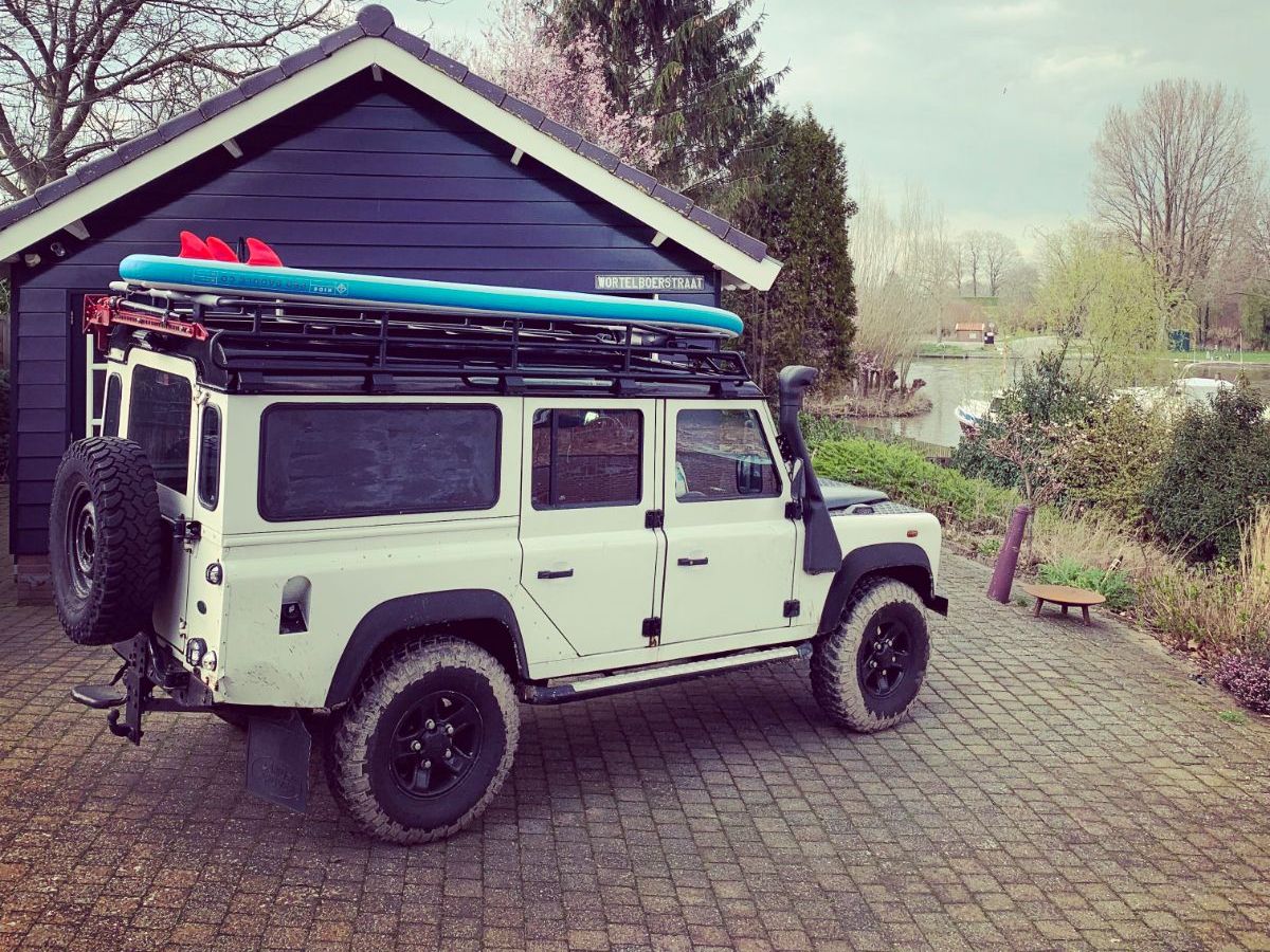 Landrover voor een schuur bij de rivier. Op het dak een SUP-board,