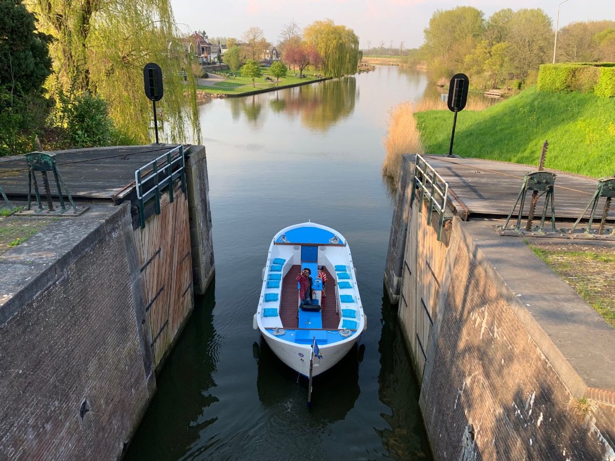 Een man in een boot die een sluis in vaart, in de achtergrond een vergezicht naar de rivier