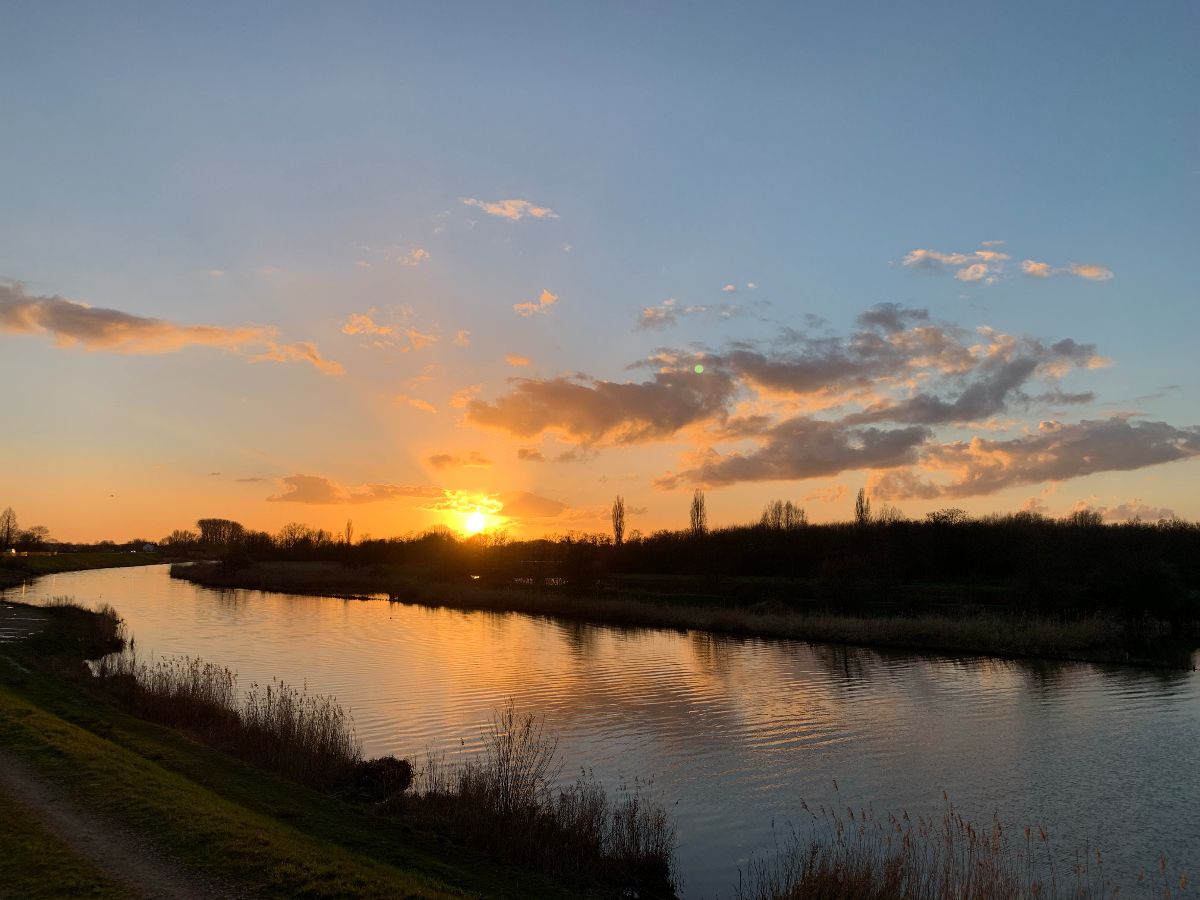 Enkele wolken in een blauwe lucht met een gouden zonsondergang met op de voorgrond een rivier die in de verte een bocht omgaat